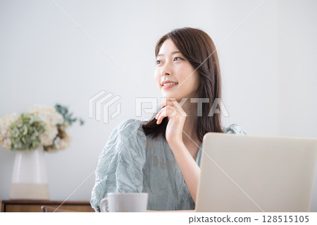 A young cute woman in casual clothes using a computer in her home room, looking up, thinking, worried pose 128515105