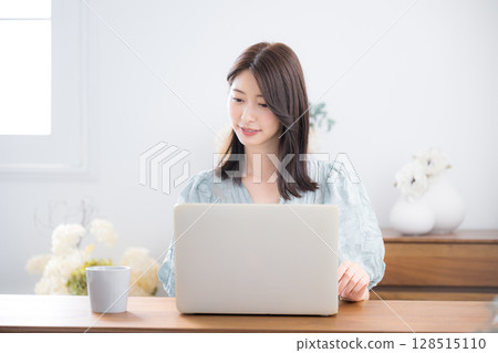 一位年輕、時尚、可愛的女士穿著休閒服，在家裡的房間裡使用電腦，低頭看著 128515110