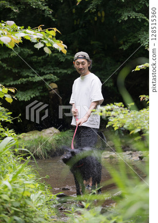 Large dog and owner playing in the river. A dog that is sensitive to heat and plays in the river in summer. Looking at the camera. Large dog and owner playing in the river. A dog that is sensitive to heat and plays in the river in summer. Looking at the camera. 128515360