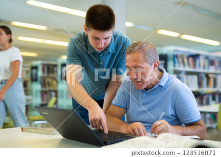 Focused male coworkers discussing remote job and searching in Internet in the library 128516071