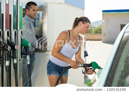 Woman refuelling her car at petrol filling station Woman refuelling her car at petrol filling station 128516190