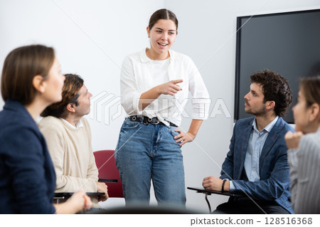 Professional business coach woman standing near interactive board and conducting training different people gathered in circle in auditorium 128516368