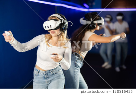 Two girls wearing virtual reality glasses participate in game with opponents 128516435