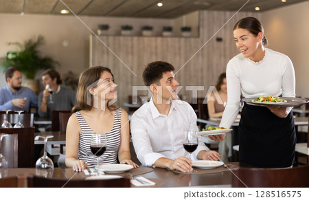 Waitress brings order to young man and woman couple Waitress brings order to young man and woman couple 128516575
