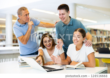 Man in casual clothes making silence gesture for young ladies using laptop in the library Man in casual clothes making silence gesture for young ladies using laptop in the library 128516668