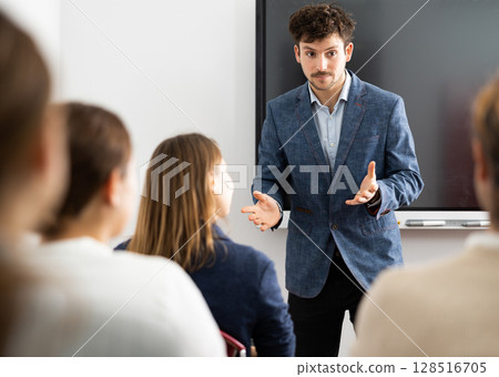 Young man standing near interactive board and communicating with adult students during advanced training courses in classroom 128516705