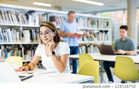 Portrait of adult latino woman studying at library using books and laptop Portrait of adult latino woman studying at library using books and laptop 128516750