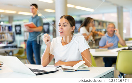 Portrait of woman studying at library using books and laptop 128516774