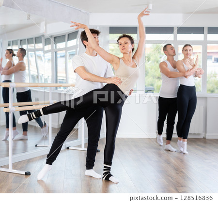 Young active man engaged in dance hall with female partner and practicing ballet arabesque pose during group class. Hobby lifestyle concept Young active man engaged in dance hall with female partner and practicing ballet arabesque pose during group class. Hobby lifestyle concept 128516836