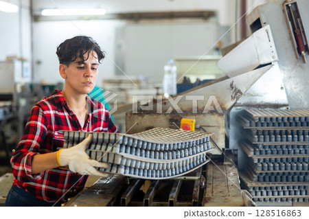 Attentive plantation female worker loading empty trays in automatic seed planting line preparing for planting seeds in greenhouse Attentive plantation female worker loading empty trays in automatic seed planting line preparing for planting seeds in greenhouse 128516863