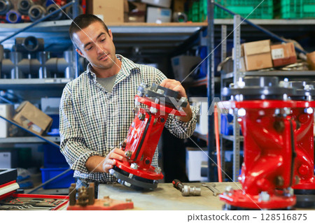 Base for the valve is installed and clamped in a vice for assembly at the factory and the worker installs and fastens components Base for the valve is installed and clamped in a vice for assembly at the factory and the worker installs and fastens components 128516875