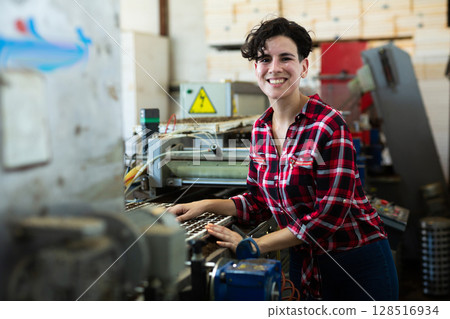 Skilled farmer woman working with automatic filling and seeding line for growing containerized seedlings of decorative plants in greenhouse Skilled farmer woman working with automatic filling and seeding line for growing containerized seedlings of decorative plants in greenhouse 128516934