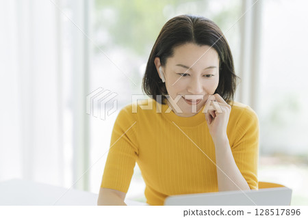 一位五十多歲的女士戴著耳機，面對著筆記型電腦 128517896