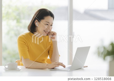 一位五十多歲的女士戴著耳機，面對著筆記型電腦 128518008