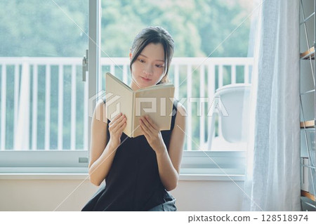 A woman reading a book at the window side A woman reading a book at the window side 128518974