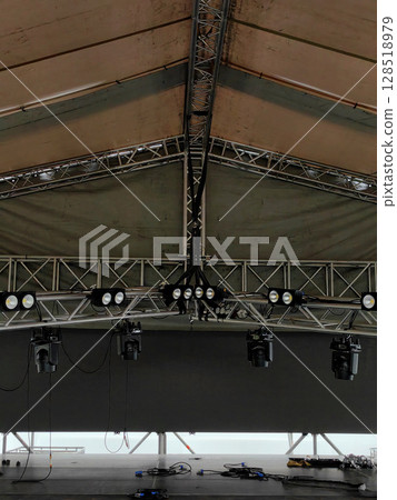 stage lights and equipment are arranged under substantial canopy at an outdoor venue. close up. stage lights and equipment are arranged under substantial canopy at an outdoor venue. close up. 128518979