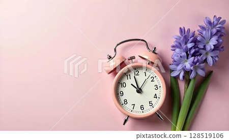 A pink alarm clock and purple flowers set against a pink backdrop, evoking the freshness of spring 128519106