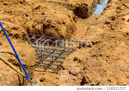 Workers prepare trench with steel reinforcement grid in construction site under construction work 128521727