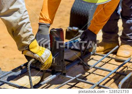 Workers collaborate to secure rebar on wooden mold at construction site under construction work day 128521733