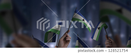 Lesotho flags in their hands on a blurred urban background Lesotho flags in their hands on a blurred urban background 128521754