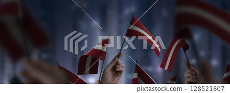 Latvia flags in their hands on a blurred urban background Latvia flags in their hands on a blurred urban background 128521807