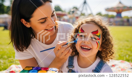 Happy mother and daughter face painting outdoors at a sunny amusement park 128522552