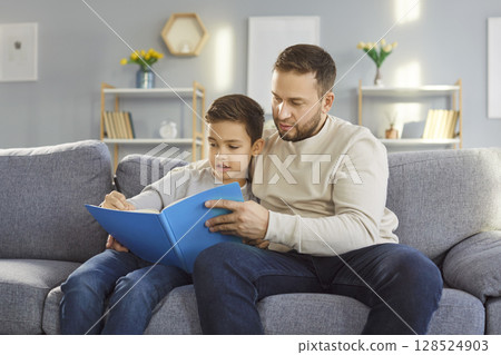 Father And Son Reading Book Together On Couch During Leisure Time At Home 128524903