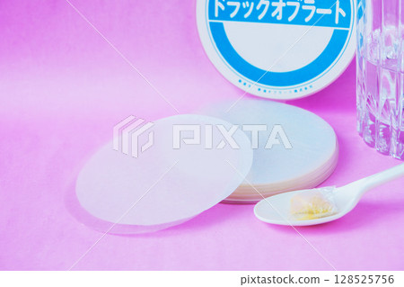 Powdered medicine wrapped in an oblate and placed on a spoon with a glass of water Powdered medicine wrapped in an oblate and placed on a spoon with a glass of water 128525756