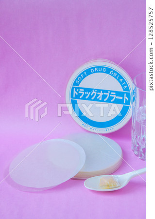 Powdered medicine wrapped in an oblate and placed on a spoon with a glass of water 128525757