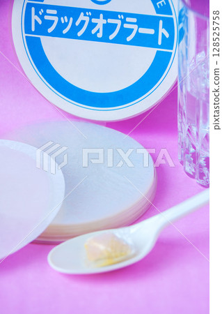 Powdered medicine wrapped in an oblate and placed on a spoon with a glass of water 128525758