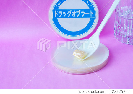 Powdered medicine wrapped in an oblate and placed on a spoon with a glass of water 128525761
