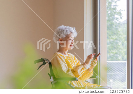 一位坐在輪椅上的老年婦女正在使用智慧型手機 128525785