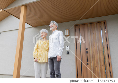 Smiling senior couple standing in front of their house Smiling senior couple standing in front of their house 128525793