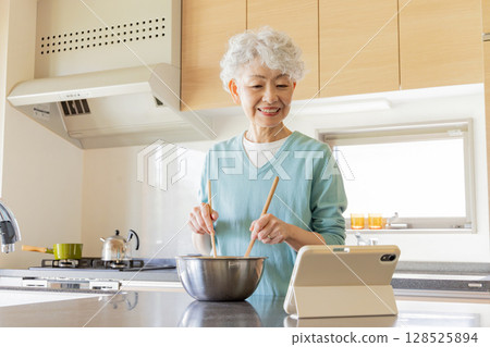 一位老年婦女一邊做飯一邊看平板電腦 128525894
