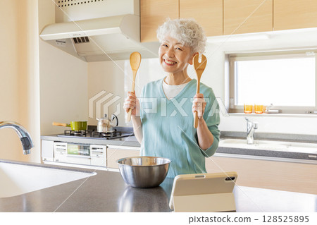 一位老年婦女一邊做飯一邊看平板電腦 一位老年婦女一邊做飯一邊看平板電腦 128525895