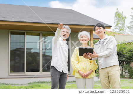 A male worker and a senior couple explaining in front of a house 128525991