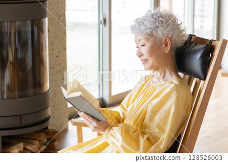 Senior woman sitting in a rocking chair reading a book 128526003