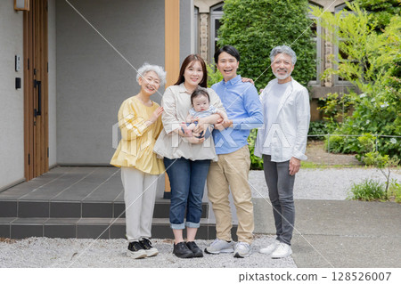 A smiling three-generation family in front of their home 128526007