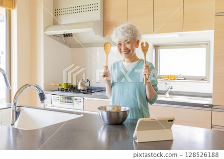 一位老年婦女一邊做飯一邊看平板電腦 一位老年婦女一邊做飯一邊看平板電腦 128526188