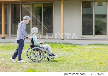 Senior couple in wheelchairs walking in front of their house 128526203