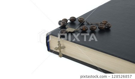 Rosary placed on top of black Bible isolated on white 128526857