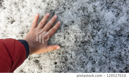 Hand touches the icy surface of Solheimajokull Glacier in Iceland, capturing a personal moment with nature's raw and melting beauty. 128527018