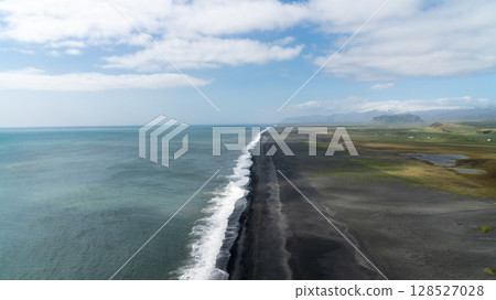 Aerial view of the black sand beach stretching along the Atlantic near Vik, Iceland, shaped by ancient volcanic forces and crashing ocean waves. 128527028