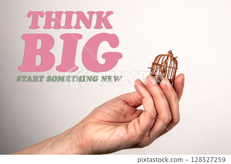 Think Big. Miniature Birdcage Held in Hand on Light Background Think Big. Miniature Birdcage Held in Hand on Light Background 128527259