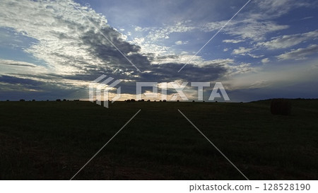 Dramatic Sky Over Rural Landscape with Hay Bale at Sunset. Serene Countryside Scene Dramatic Sky Over Rural Landscape with Hay Bale at Sunset. Serene Countryside Scene 128528190
