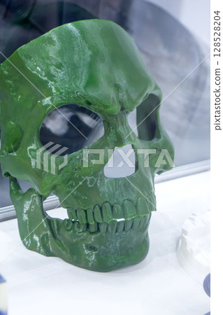 Art object printed on 3D printer. Model created on 3D printer from green molten plastic. Creative shape mask human skull printed on 3D printer. Additive high-tech technology. 3D printing technology 128528204