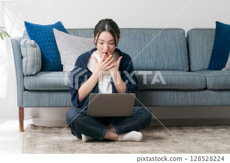 Surprised woman looking at a computer in the living room Surprised woman looking at a computer in the living room 128528224