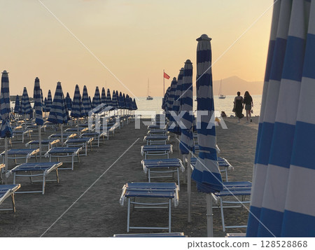 Beach umbrellas and sun loungers by sea. Sunset in summer, vacation in Liguria, Italy. Background for text. 128528868