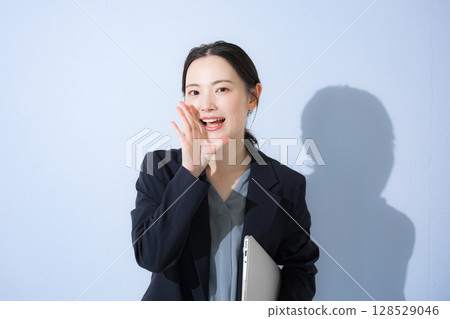 A young cute woman in a suit standing with a laptop cheering and calling out secrets, upper body business, light blue 128529046