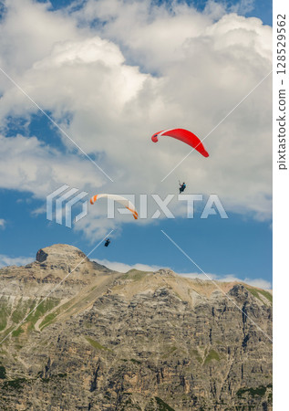 Paragliders Soaring Over Rocky Alpine Peaks Under Blue Sky and White Clouds. High quality photo 128529562
